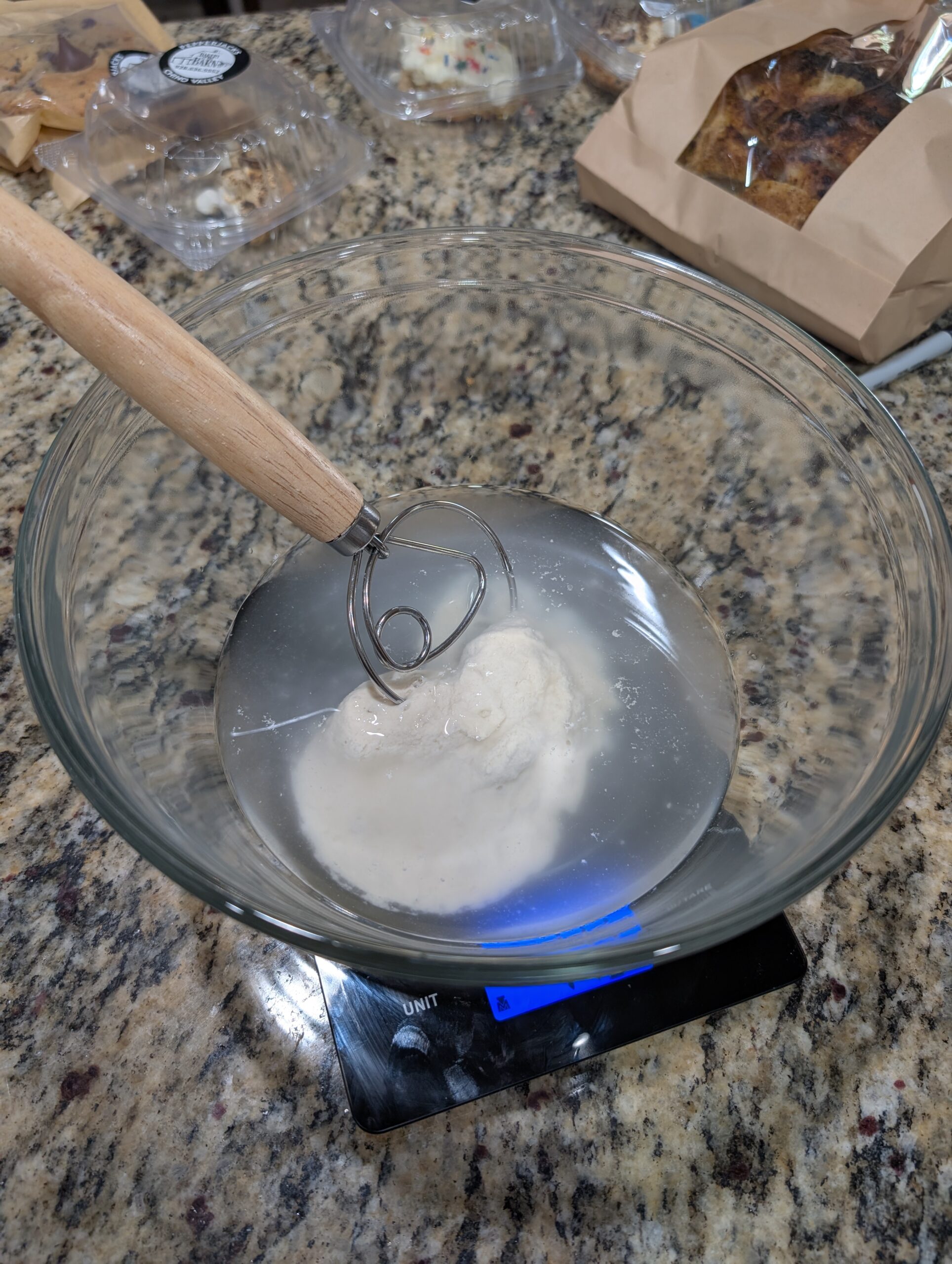 Whisking water in a clear glass mixing bowl to combine with sourdough starter