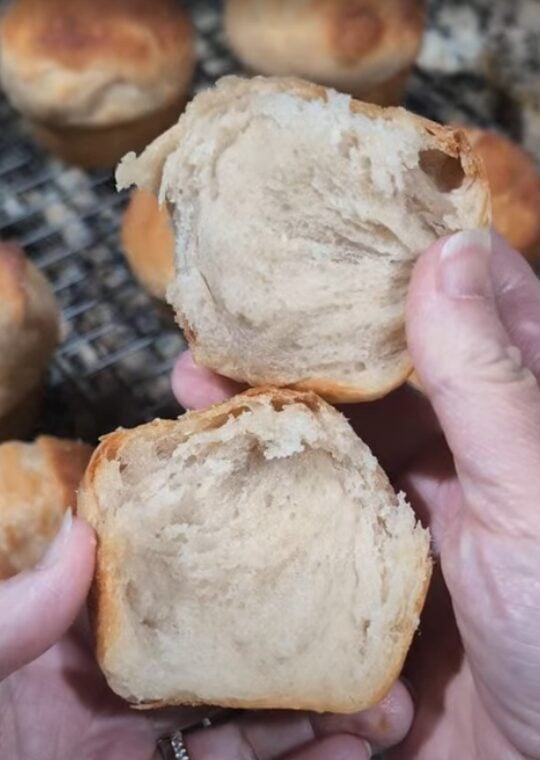 Hand pulling apart a buttery sourdough pull-apart roll showing the soft layered interior